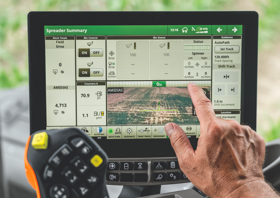 Mano de operador utilizando la pantalla interactiva G5 de John Deere, parte de los Kits Esenciales Salfa, que muestra datos en tiempo real sobre la aplicación de insumos y el guiado de precisión en el campo.